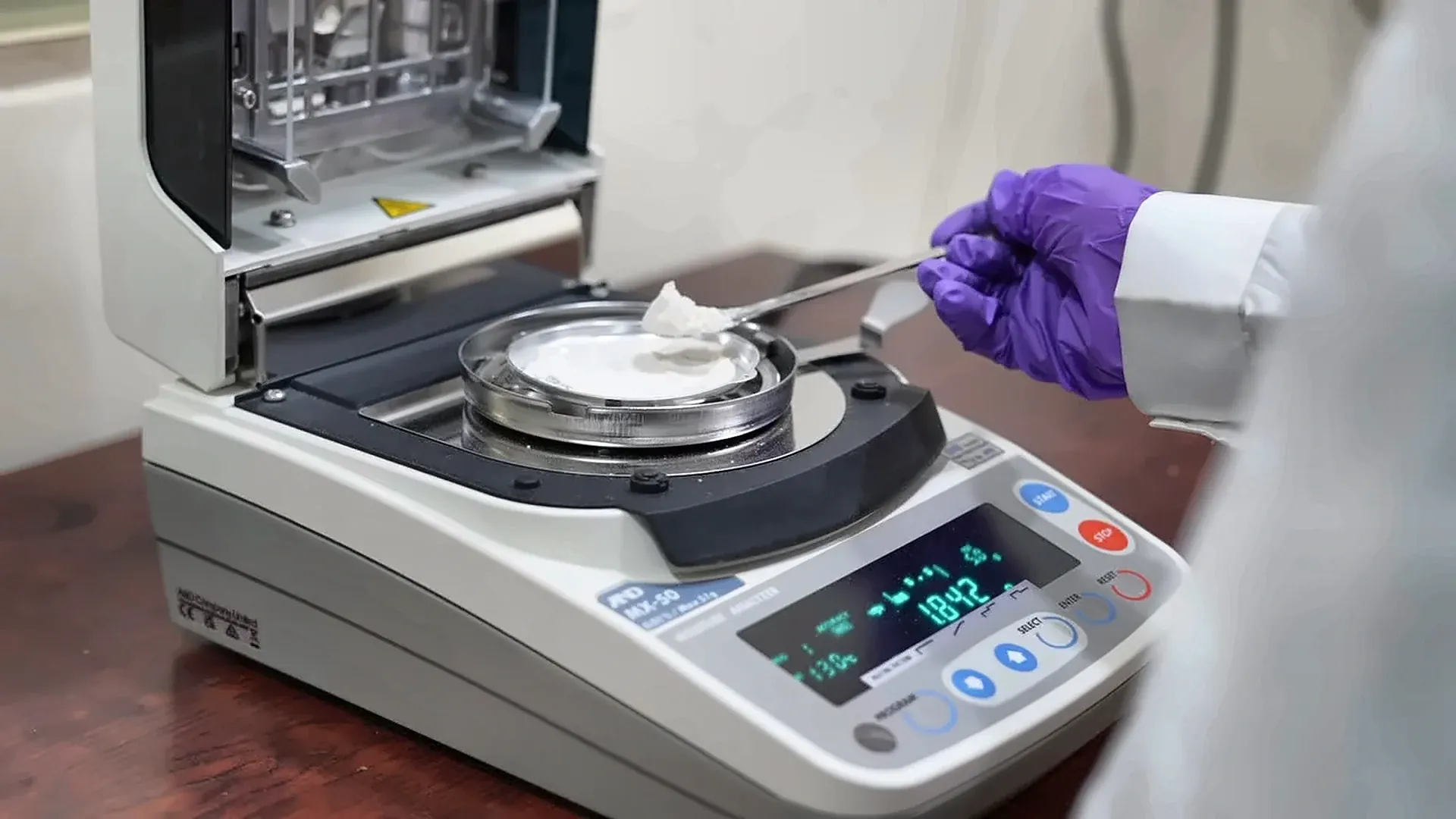 A lab technician in gloves placing a flour sample on a moisture analyser
